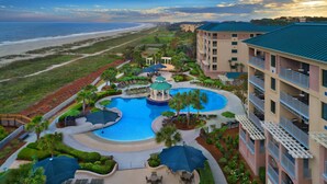 Un resort con piscina central, vista a la playa y un edificio de varios pisos con balcones.