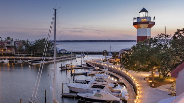 Un port de plaisance avec des bateaux amarrés, un phare et un bâtiment doté d’une terrasse.