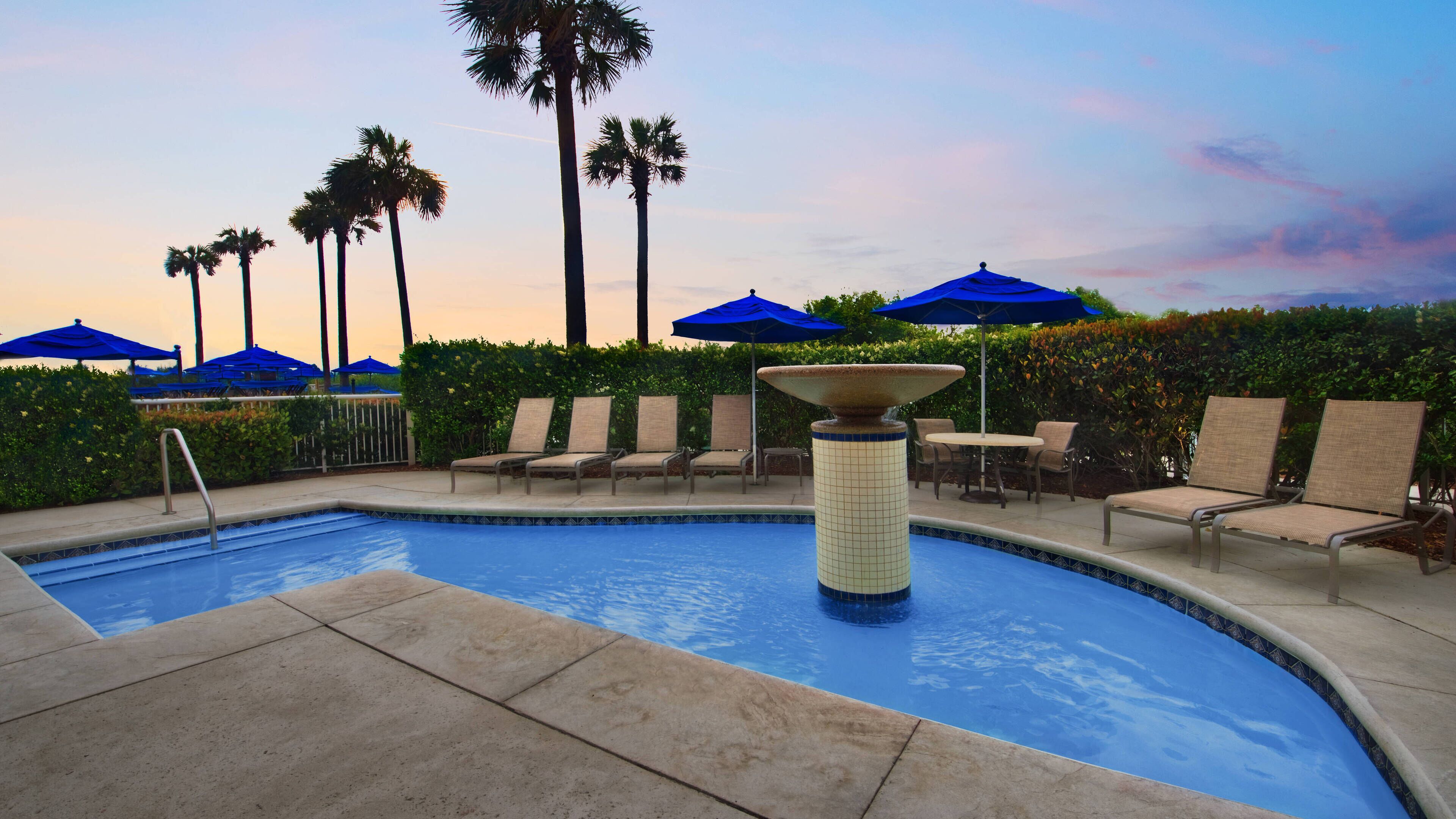 A pool area with lounge chairs, umbrellas, and a decorative fountain.