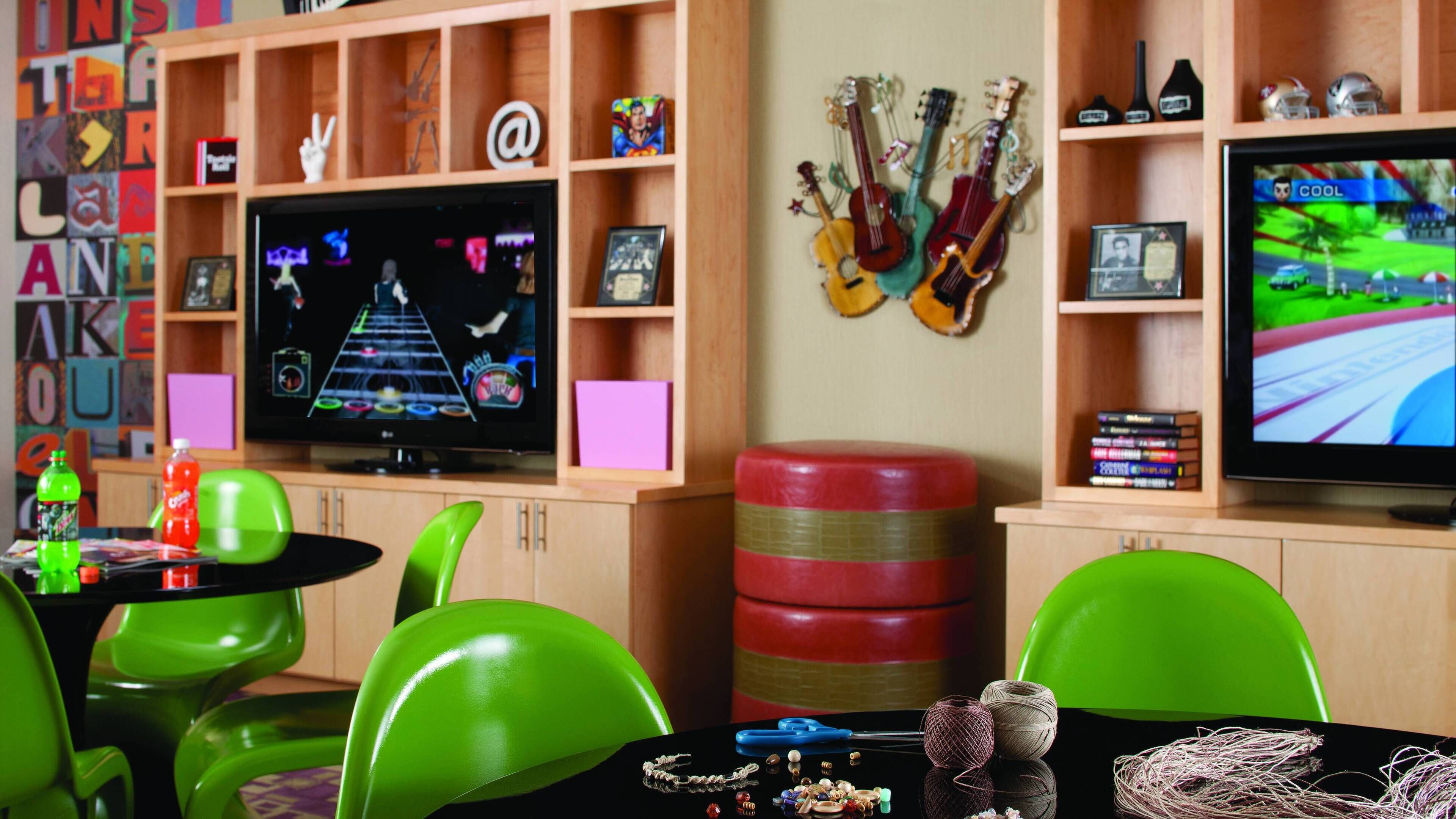 Una stanza con sedie verdi, una TV che mostra un videogioco, chitarre appese al muro e mensole piene di oggetti vari.