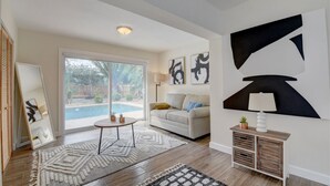 A modern living room with a large window, a white sofa, abstract wall art, and a pool view. - Bliss Near Beach w/ Guest House + Salt Heated Pool (Boynton Beach)