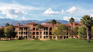 A large, multi-story hotel with a red-tiled roof and multiple balconies, surrounded by a well-maintained lawn and palm trees, with mountains in the background. - 2 Bedroom - Marriott's Shadow Ridge I - The Villages - Full Resort Access (Palm Desert)