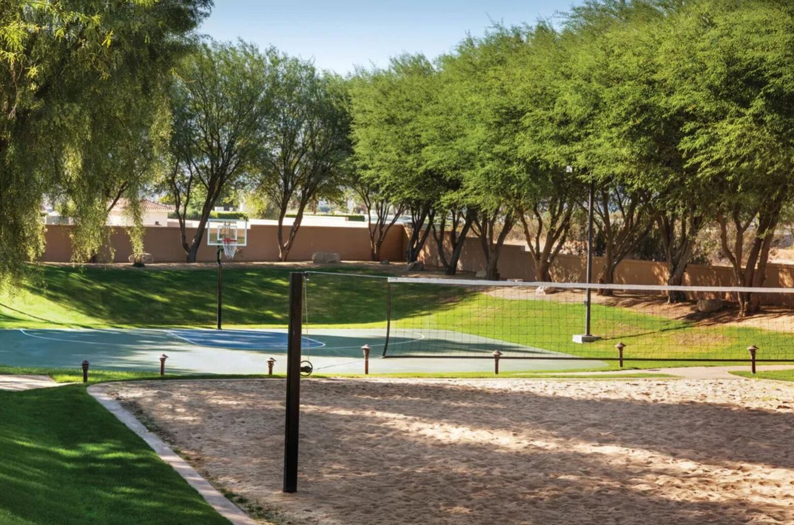 Una cancha de tenis rodeada de árboles y un aro de baloncesto.