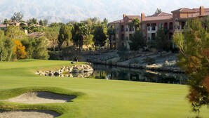 Un terrain de golf avec un étang, une personne jouant au golf et, au fond, un bâtiment avec un toit rouge.