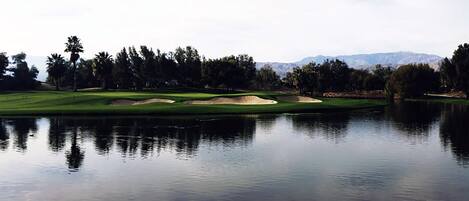 Un lago tranquilo que refleja un campo de golf con bunkers de arena y árboles.