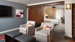 A hotel room with a large bed, two armchairs with colorful cushions, a flat-screen TV, a painting on the wall, and a sliding door leading to a bathroom. - 2 Bedroom - Marriott's Shadow Ridge II - The Enclaves - Full Resort Access (Palm Desert)