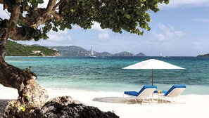 A beach with two lounge chairs under a white umbrella, a rocky foreground, and a sailboat in the background. - 2 Bedroom - The Ritz-Carlton Club, St. Thomas - Full Resort Access (St Thomas)