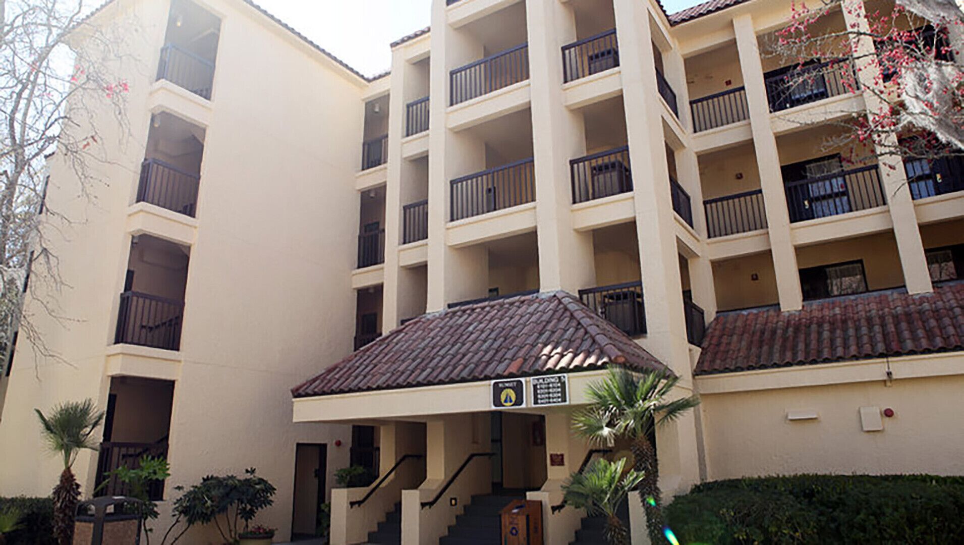 A multi-story building with balconies, a covered entrance, and a sign indicating a parking area.