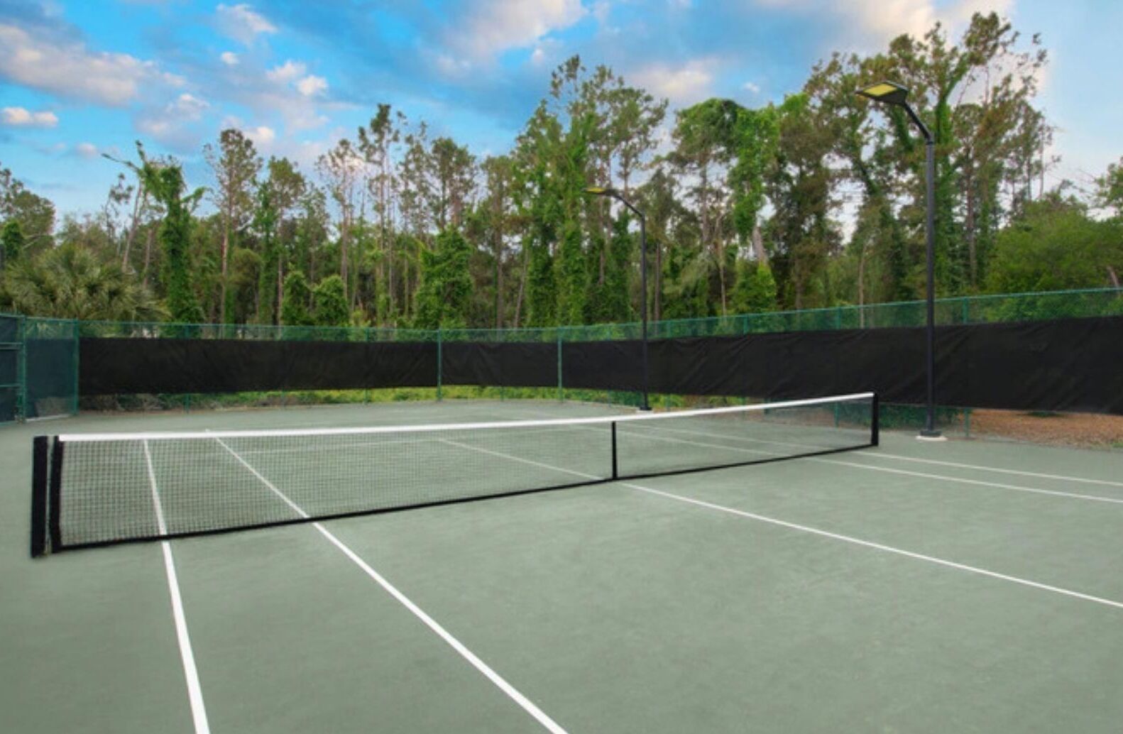 Un court de tennis avec un filet, entouré d’une clôture et d’arbres.