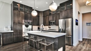 A modern kitchen with dark wood cabinets, stainless steel appliances, and a central island with bar stools. - Gorgeous Jordanelle Lake Property - 4BD/3.5BA (Hideout)