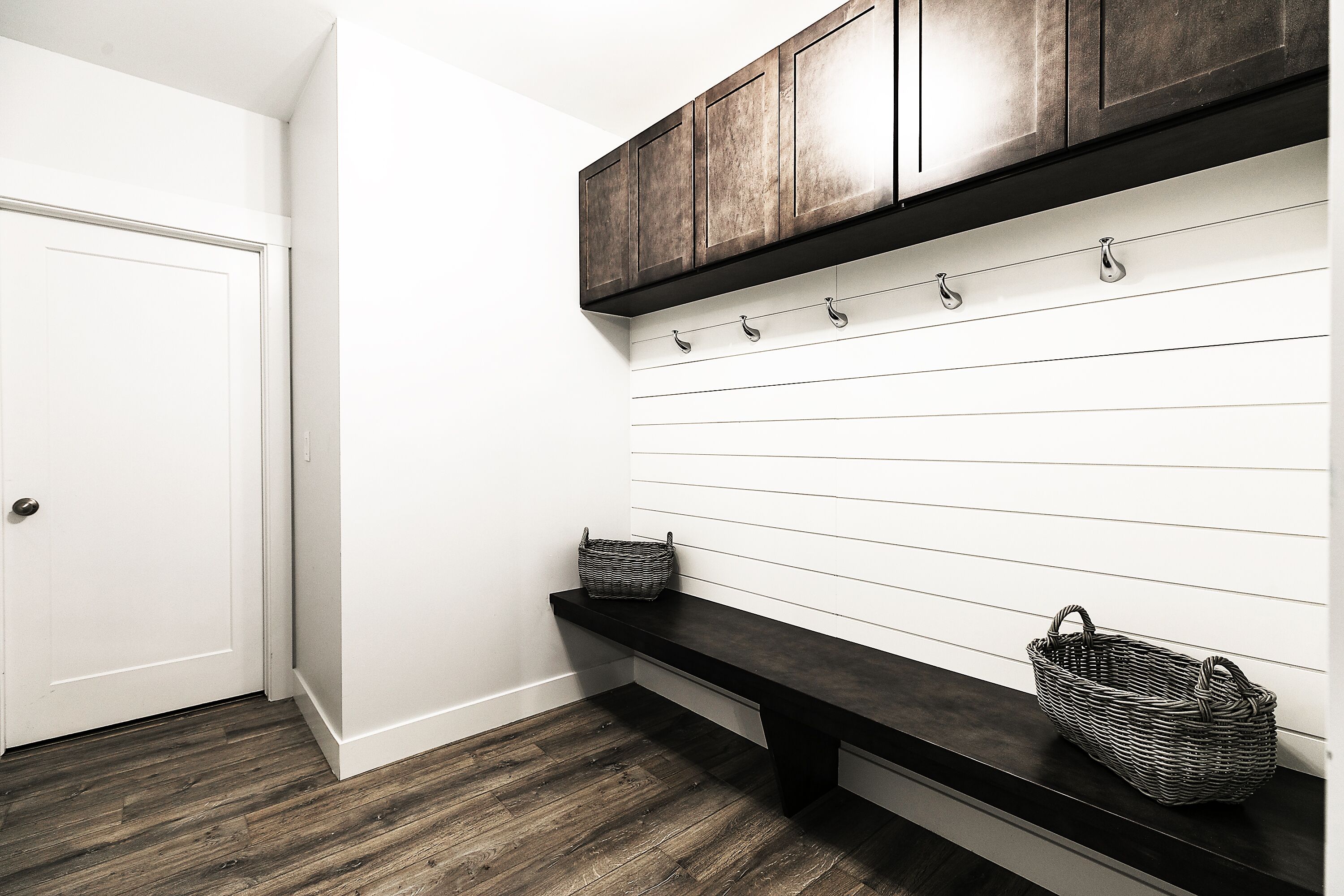 Un pasillo con una puerta blanca, un banco de madera oscura y una cesta fijada a la pared.
