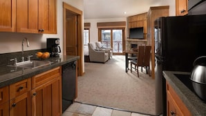 Una cocina con armarios de madera, encimera de granito y lavavajillas integrado. Hay una zona de comedor con mesa y sillas, y un ventanal con vistas al exterior.