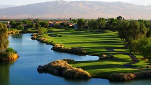 Un parcours de golf avec une rivière, des maisons et des montagnes en arrière-plan.