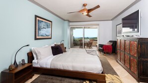 A bedroom with a bed, a ceiling fan, a TV, a sliding glass door to a balcony, and a wooden cabinet. - Oceanfront Coral Reef (Solana Beach)