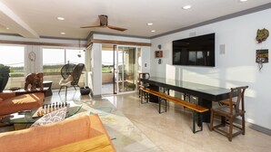A spacious living area with a glass coffee table, a sofa, a dining table with benches, and a ceiling fan. - Oceanfront Coral Reef (Solana Beach)