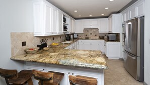 A kitchen with white cabinets, a granite countertop, and stainless steel appliances. - Oceanfront Coral Reef (Solana Beach)