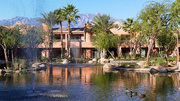 A hotel with a water feature, palm trees, and mountains in the background.