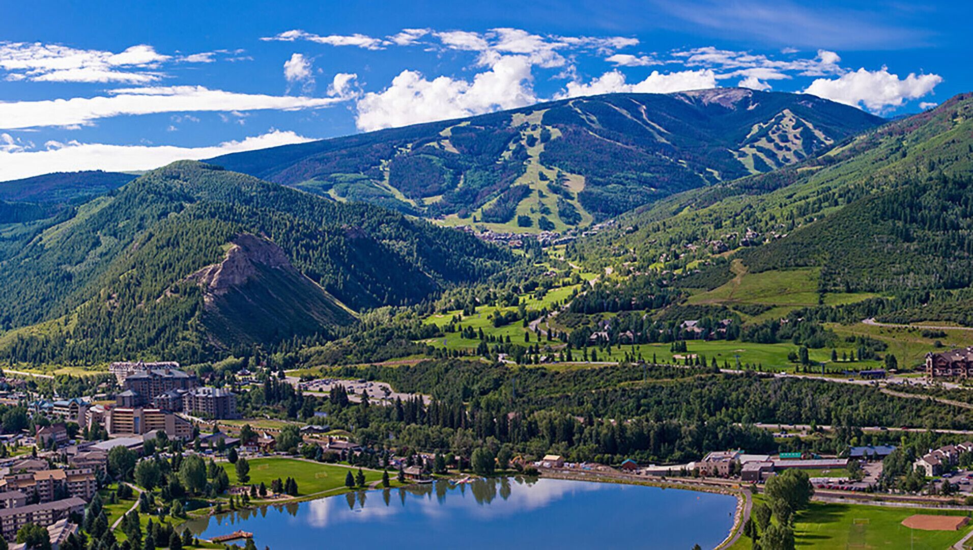 Un paysage montagneux avec un lac, des bâtiments et un ciel dégagé.