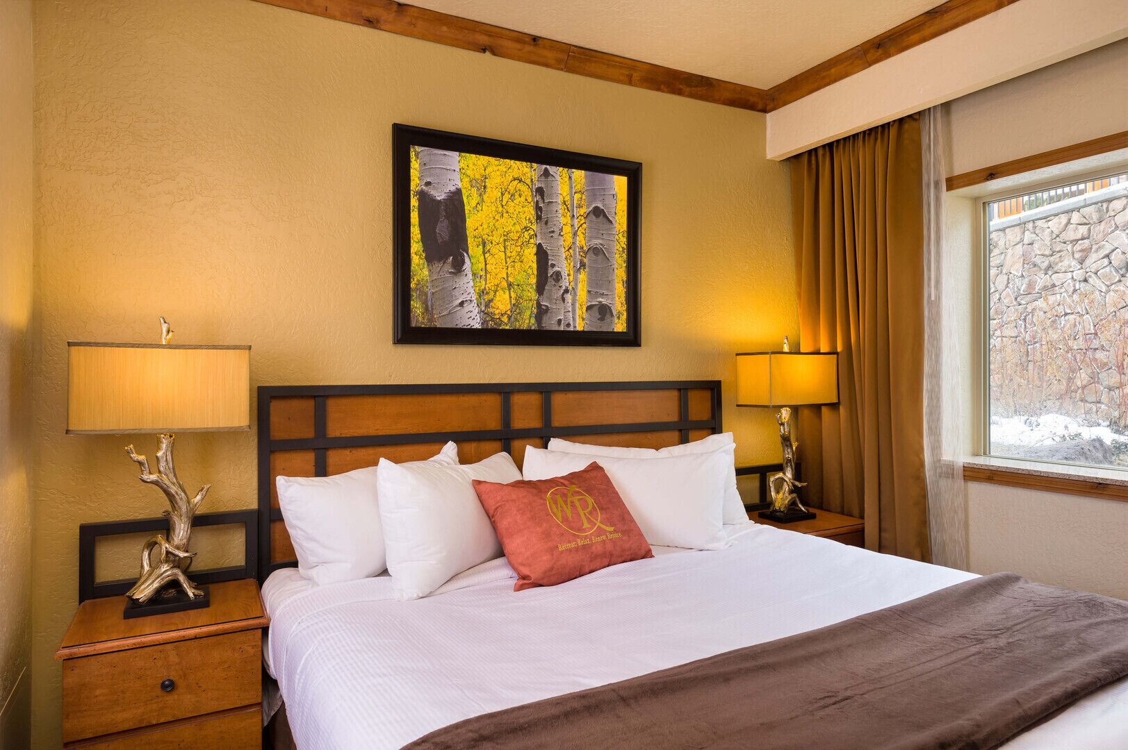 A hotel room with a large bed, two bedside tables with lamps, a framed artwork above the bed, and a window with curtains.