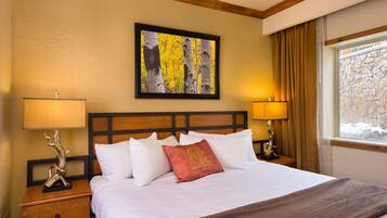 A hotel room with a large bed, two bedside tables with lamps, a framed artwork above the bed, and a window with curtains.