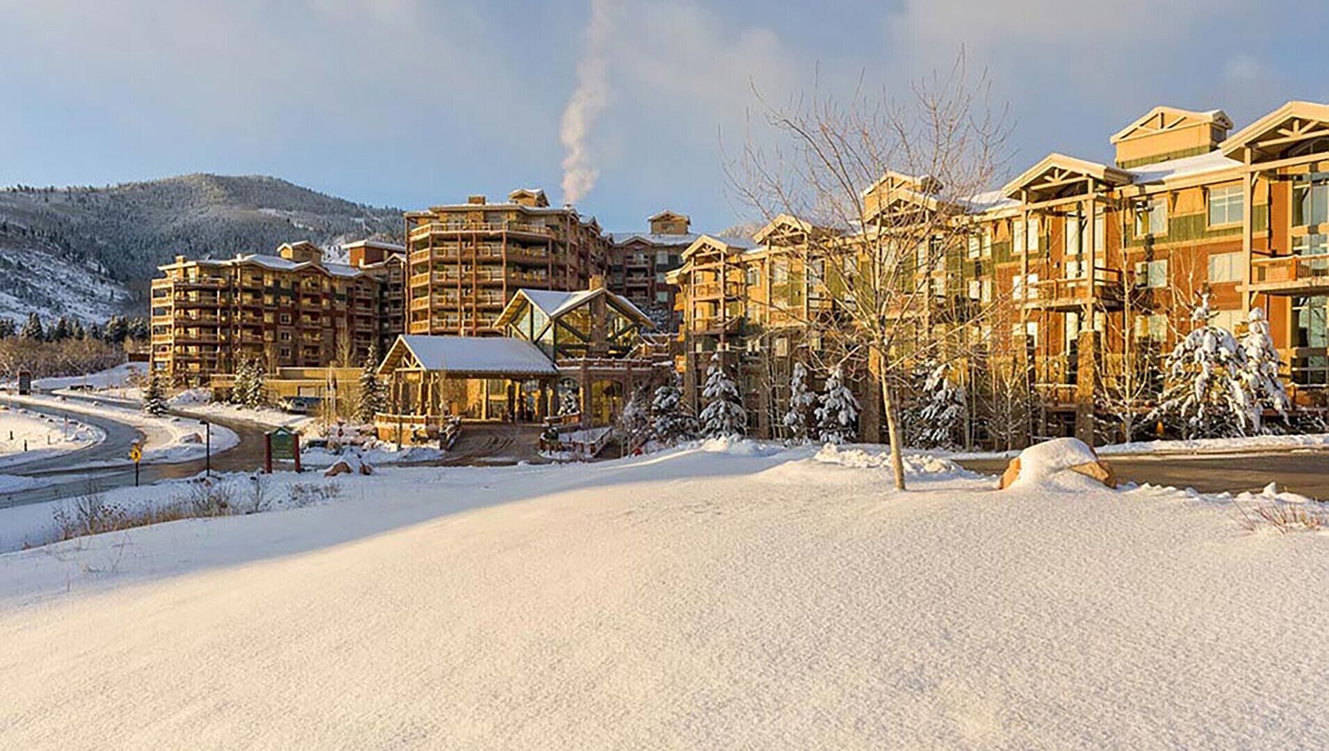 A snow-covered resort with multiple buildings, including a lodge with a prominent chimney emitting smoke.