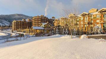 A snow-covered resort with multiple buildings, including a lodge with a prominent chimney emitting smoke.