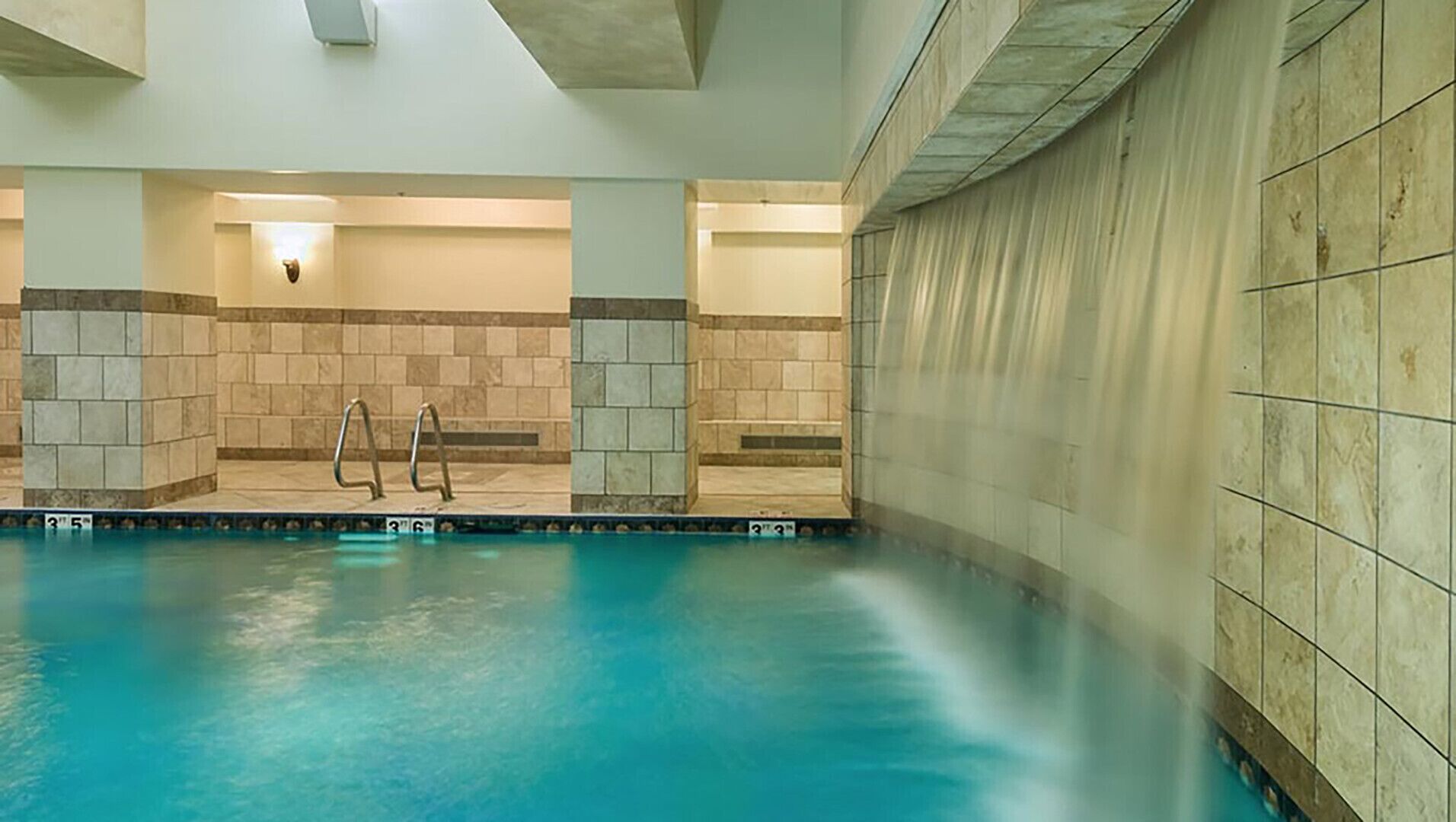 An indoor swimming pool with clear water, tiled walls, and a simple metal ladder.