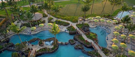 Un resort con varias piscinas, palmeras y un campo de golf al fondo.