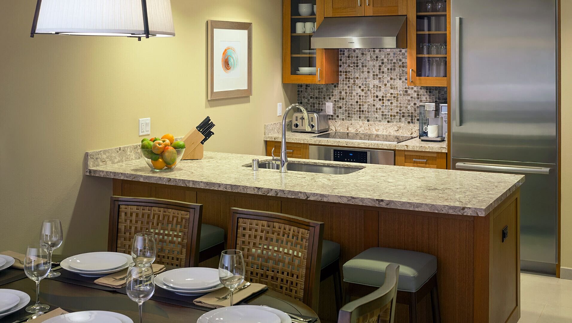 A modern kitchen with a marble countertop, a built-in island, and a stainless steel refrigerator.