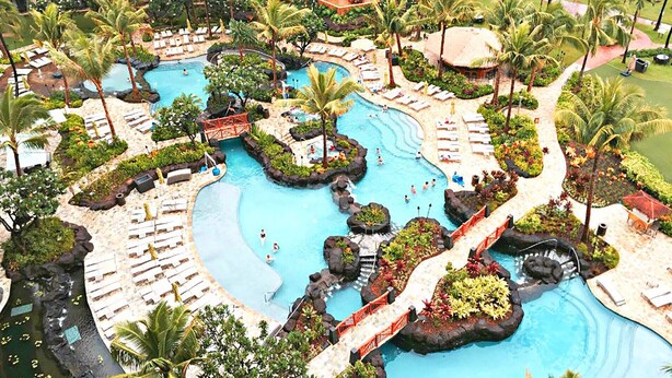 Un resort con varias piscinas, palmeras y zonas de descanso.