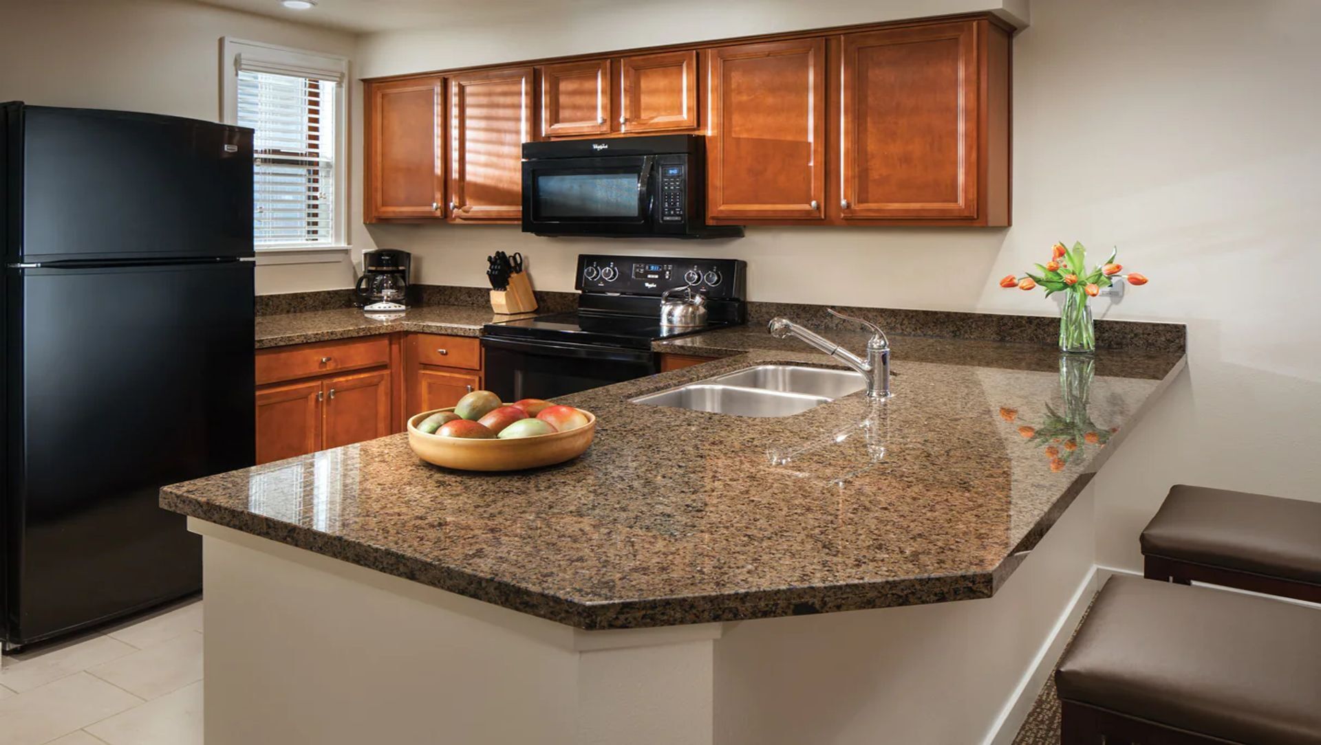 A kitchen with granite countertops, a black refrigerator, wooden cabinets, a microwave, a stove, and a sink.