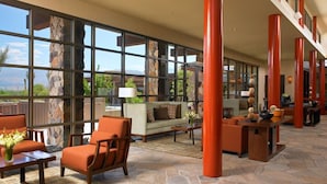 Eine geräumige Lobby mit großen Fenstern, einem Steinkamin und einer Sitzecke mit orangefarbenen Stühlen und einem Sofa.