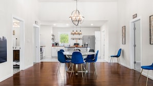 Eine moderne Küche mit Essbereich, ausgestattet mit einem Chandelier, weißen Schränken und blauen Stühlen.