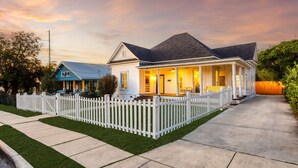 Ein zweistöckiges Haus mit Veranda, weißem Zaun und gepflegtem Rasen.