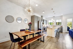 A modern kitchen with a central island, bar stools, and a dining area with a wooden table and benches. - Stay in Luxury @ The Pearl ~ .5M to Riverwalk (San Antonio)