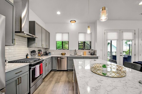 A modern kitchen with grey cabinets, stainless steel appliances, and a marble countertop.