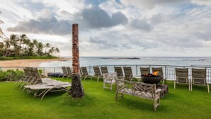 A beachside lounge with a fire pit and lounge chairs, overlooking the ocean.
