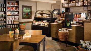A coffee shop interior with a display of coffee beans, a pastry case, and a seating area with a table and chairs.