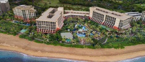 Un resort con varias construcciones, un área de piscina central y una playa.