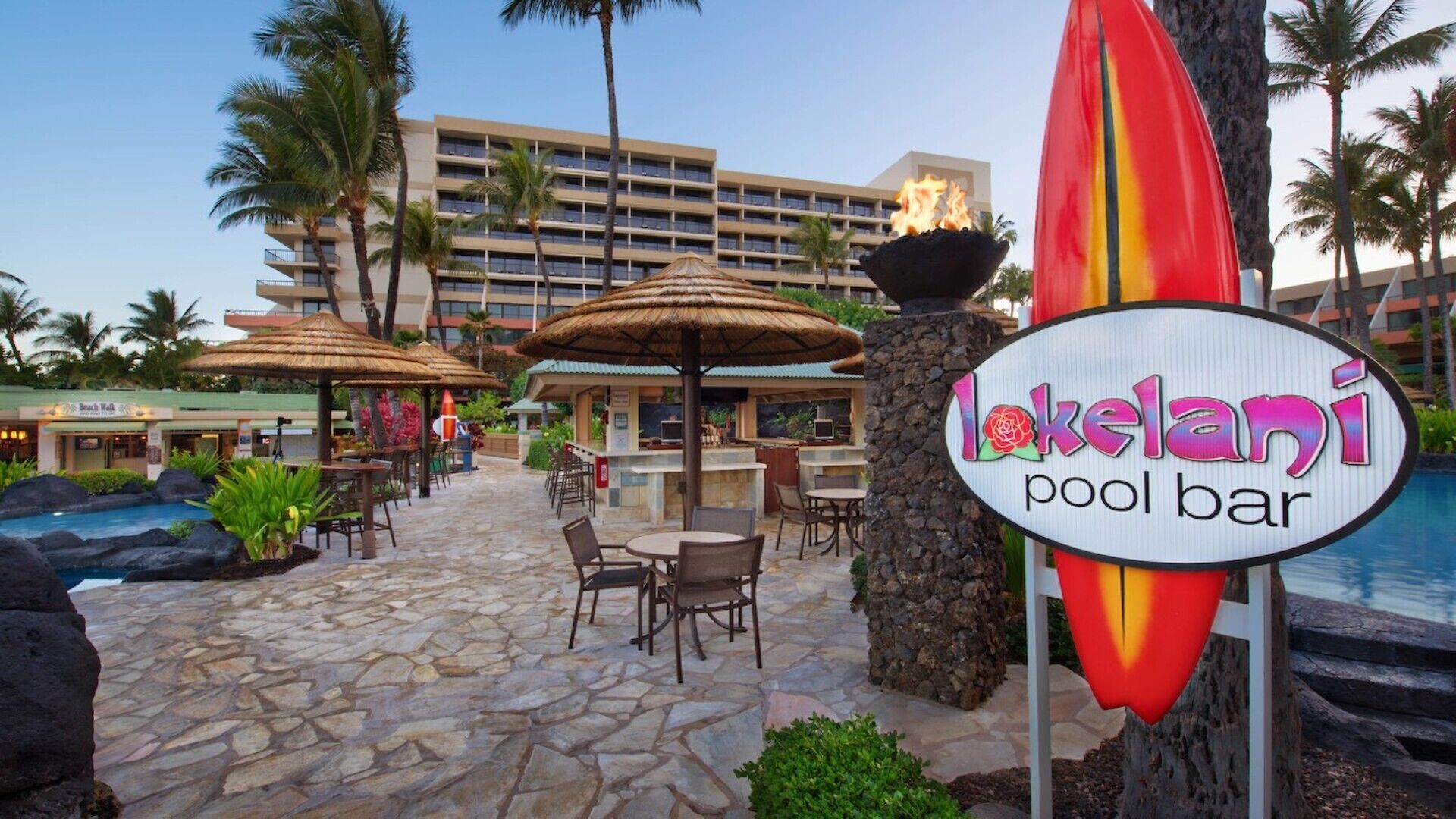 A pool bar area with outdoor seating, a sign for 'Lokelani pool bar', and a building in the background.