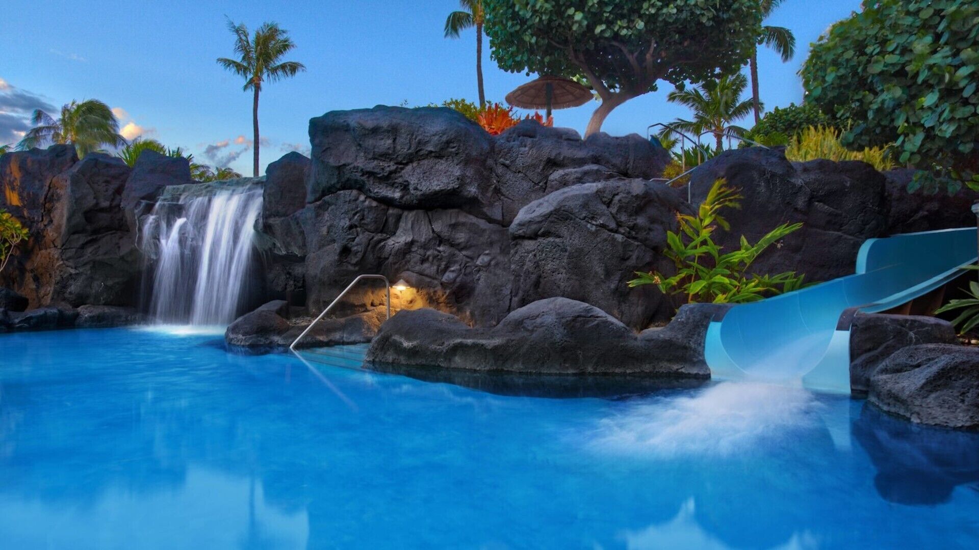 Una piscina con cascada, rodeada de rocas y palmeras.