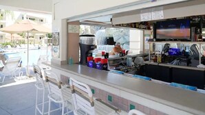 Un bar junto a la piscina con mostrador, taburetes y una pantalla de televisión.