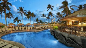 A poolside area with lounge chairs and umbrellas, palm trees, and a bar area.