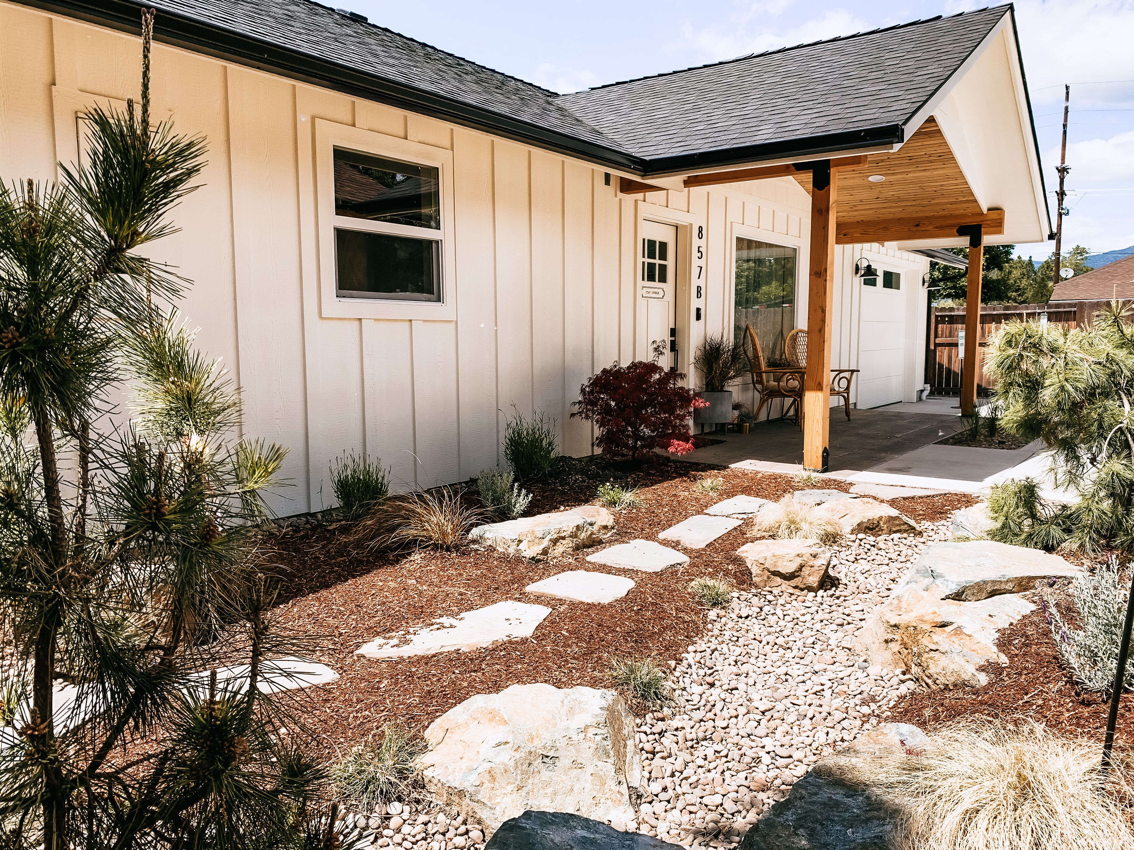 A house with a covered porch, a stone pathway, and a variety of plants.