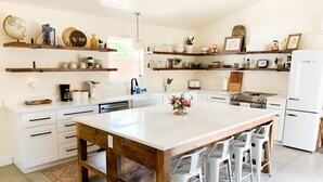 A modern kitchen with a central island, white cabinetry, and a variety of decorative items on shelves. - Cottage with gated driveway near downtown & river (Grants Pass)