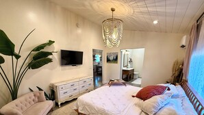 A bedroom with a bed, a dresser, a TV, a chandelier, and a large plant. - Cottage with gated driveway near downtown & river (Grants Pass)