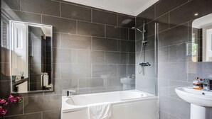 Ein modernes Badezimmer mit einer großen Badewanne, einer ein Glas abgeschirmten Dusche und einem weißen Waschbecken.