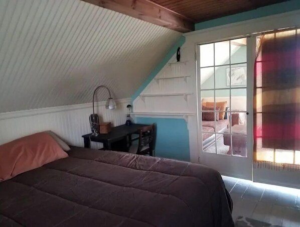 A bedroom with a bed, a desk, a lamp, and a window with a view of a balcony.