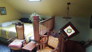 Ein gemütliches Zimmer mit einem Bett, einem Holzstuhl, einem kleinen Tisch und einem Buntglasfenster.