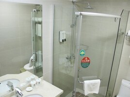 Un baño moderno con ducha de vidrio, lavamanos con artículos de aseo y un inodoro.